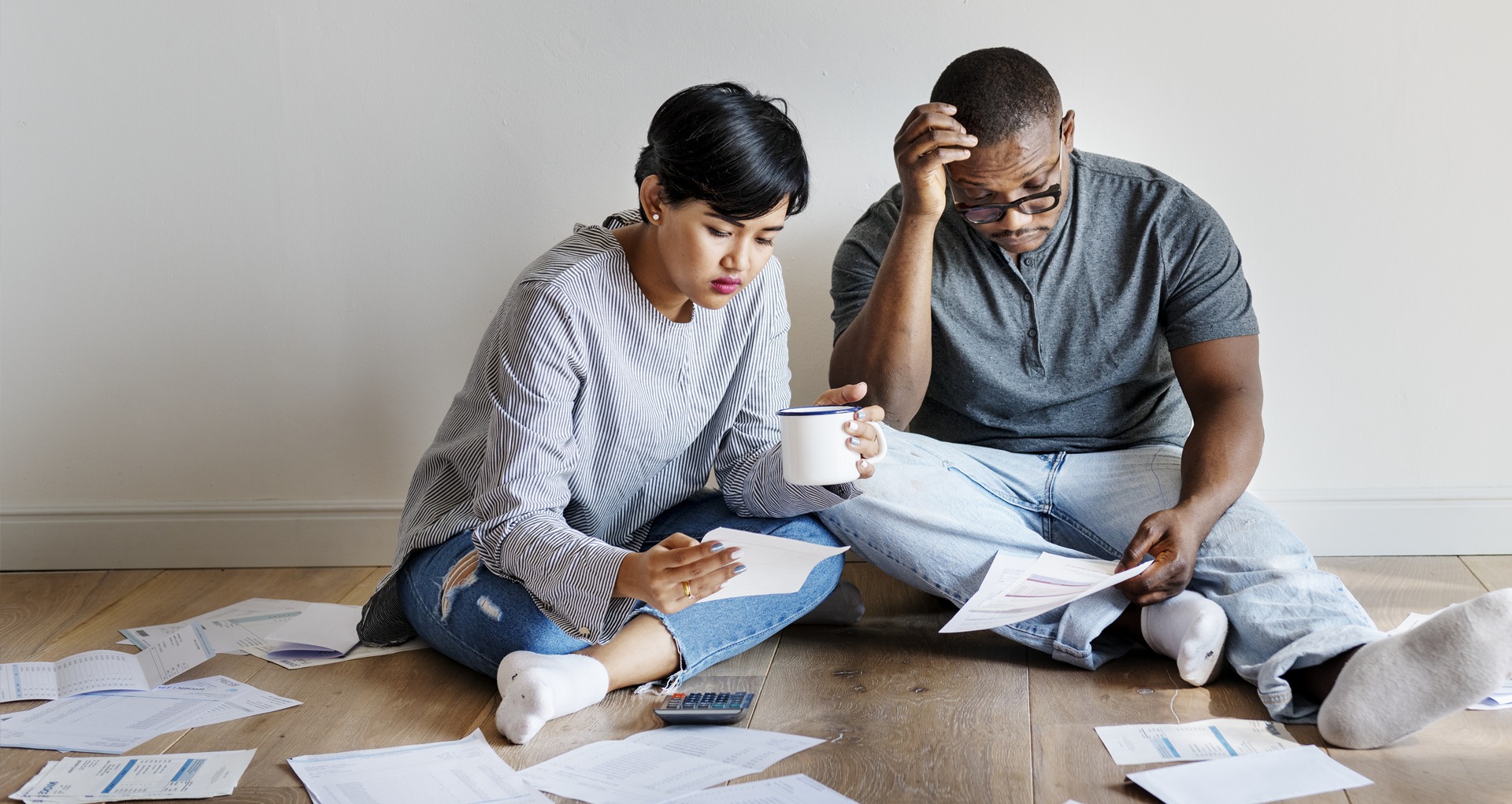 Worried couple sitting on floor surrounded by bills.